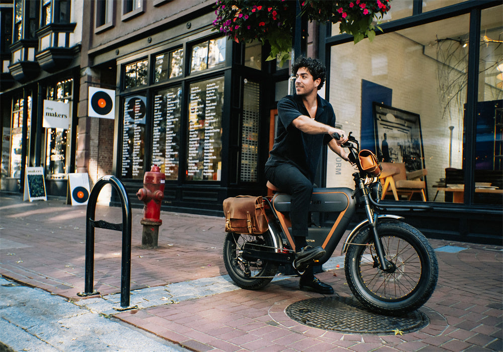 Man sitting on a RICTOR K1 e-bike in front of a city shop, with leather saddlebags and a relaxed vibe.